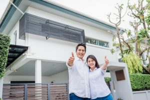 Happy Asian couple with thumb up standing together in front of thier house